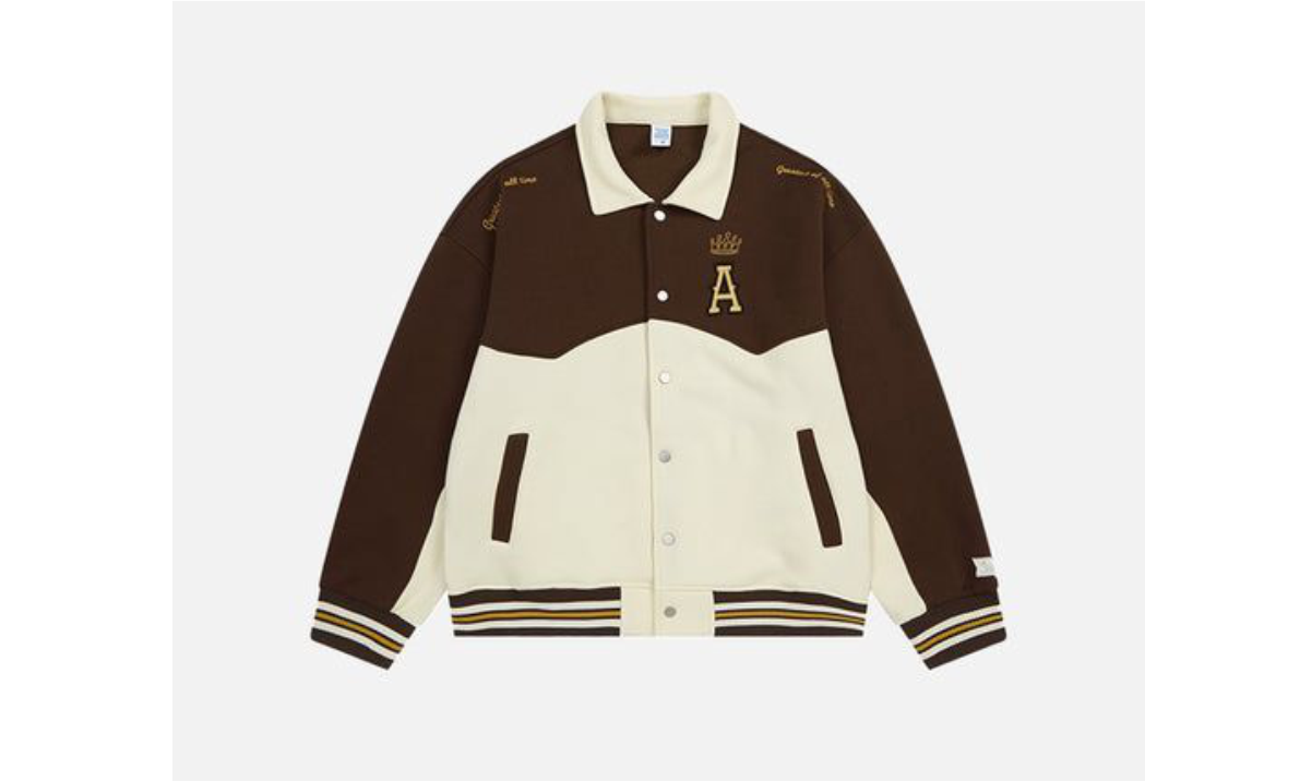 Jaket varsity coklat tua dengan aksen krem dan patch huruf A, difoto datar di latar abu muda