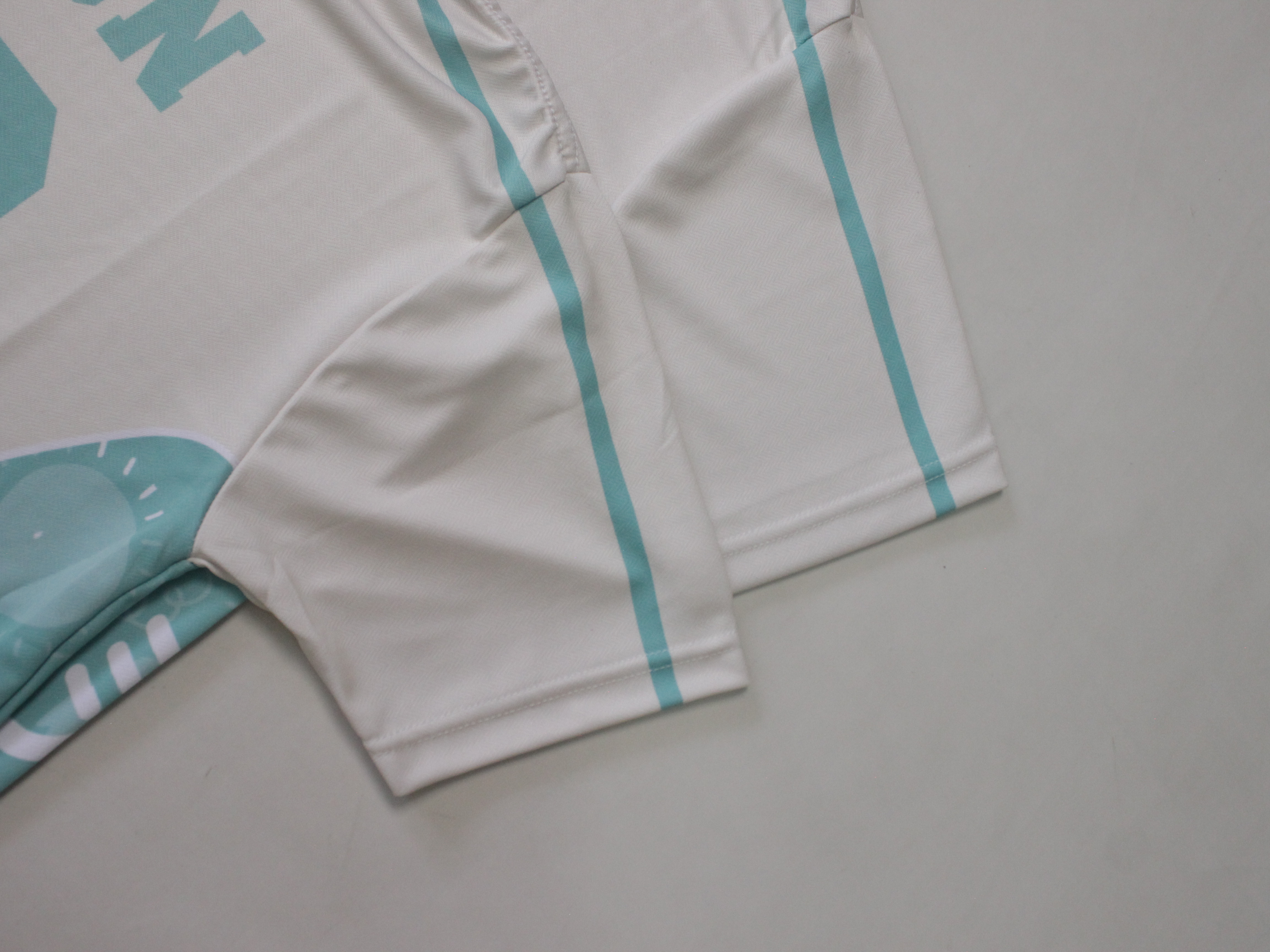 Detail lengan dan badan jersey krem dengan cetakan sublimasi tosca pada lipatan kain