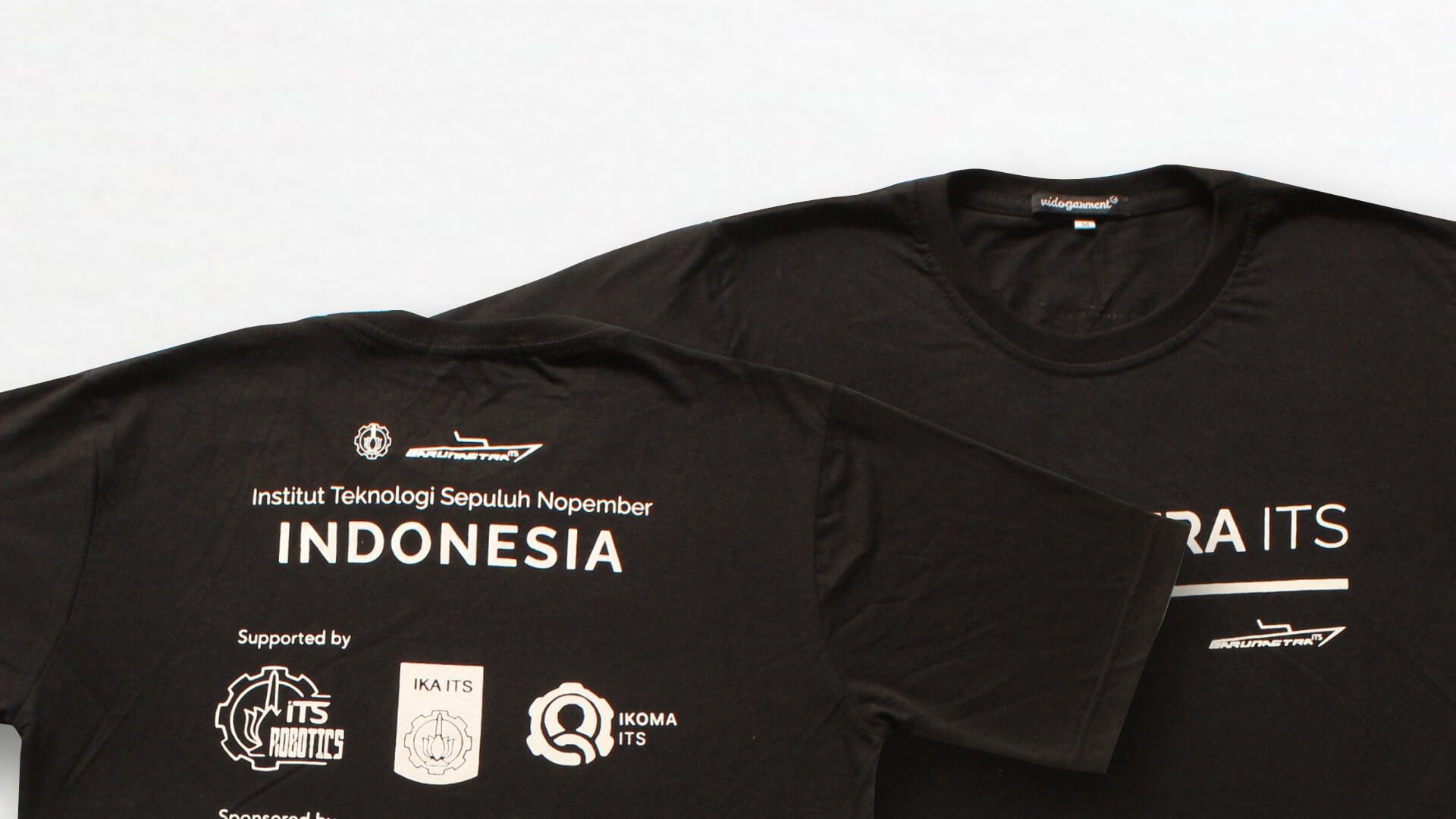 Dua kaos hitam bersablon putih dibentangkan rata