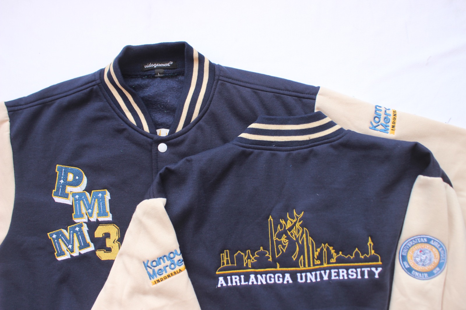 Dua jaket varsity navy berlengan krem dengan bordir punggung dari produksi pesanan angkatan