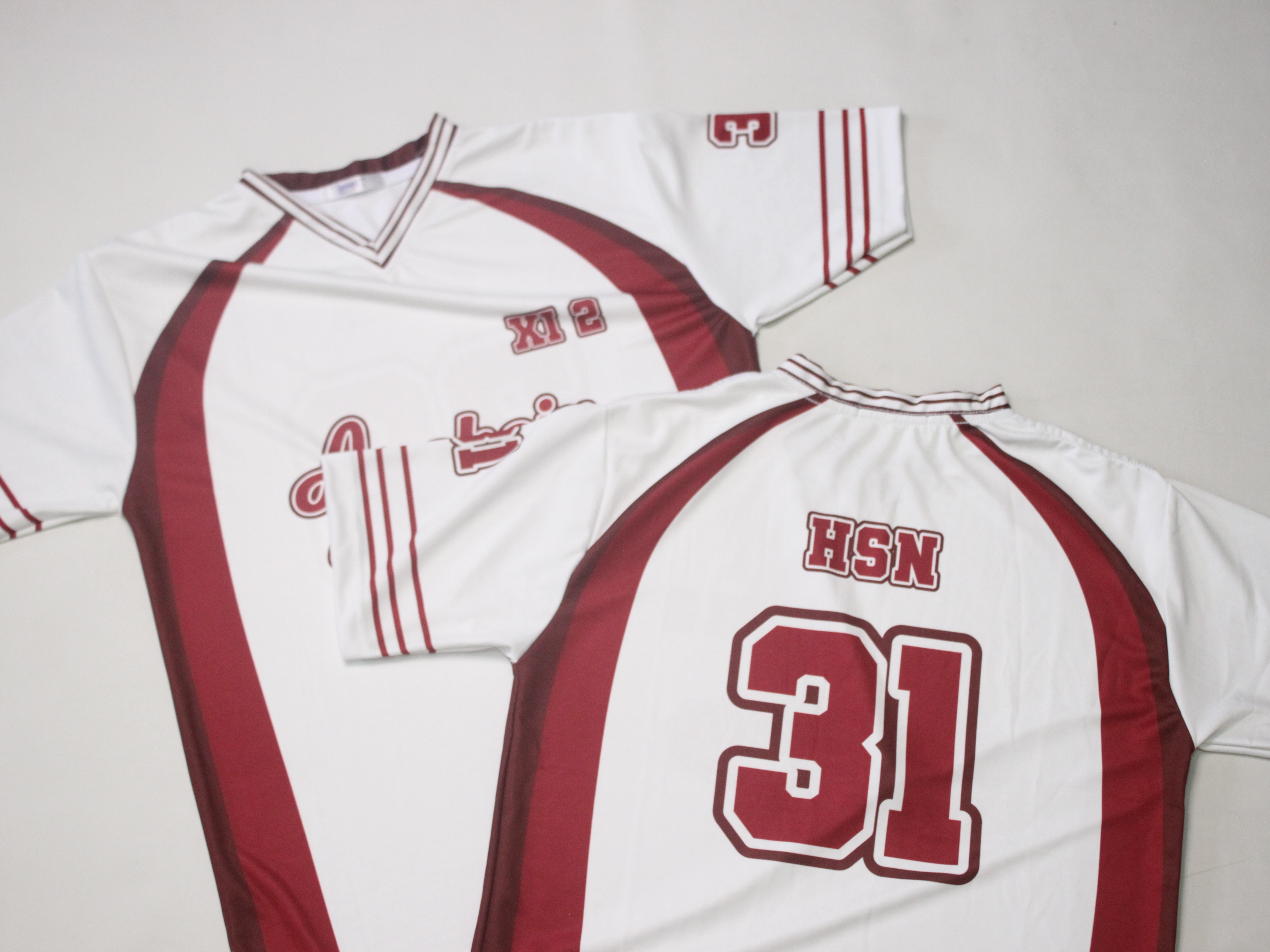 Dua jersey custom dengan nama dan nomor punggung hasil cetak sublimasi tergeletak di permukaan abu-abu
