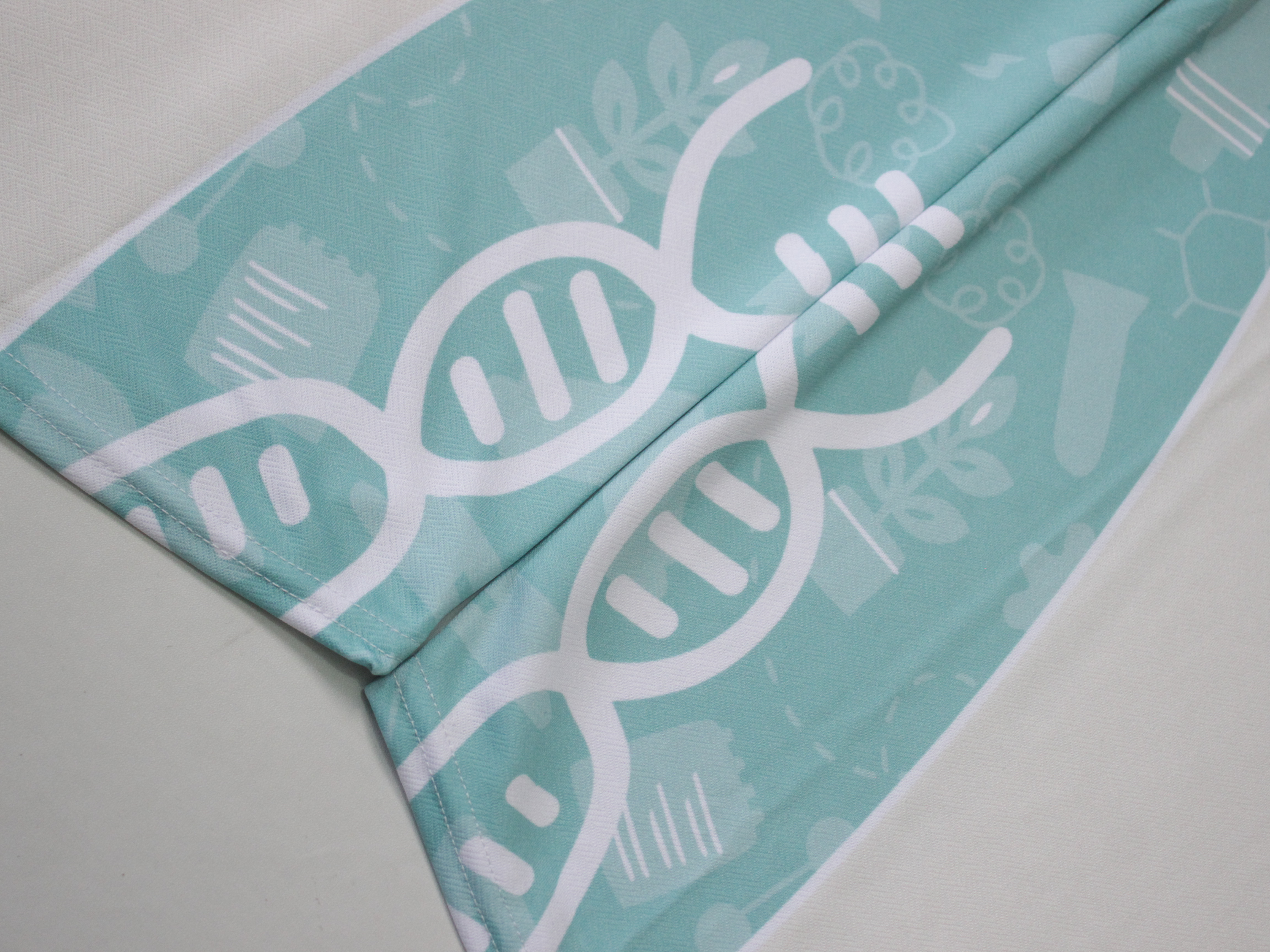 Motif cetak putih pada kain jersey tosca terlihat dari dekat; tekstur rajutan benang masih tembus di area tercetak karena warna sublimasi meresap ke dalam kain, bukan menempel di permukaan
