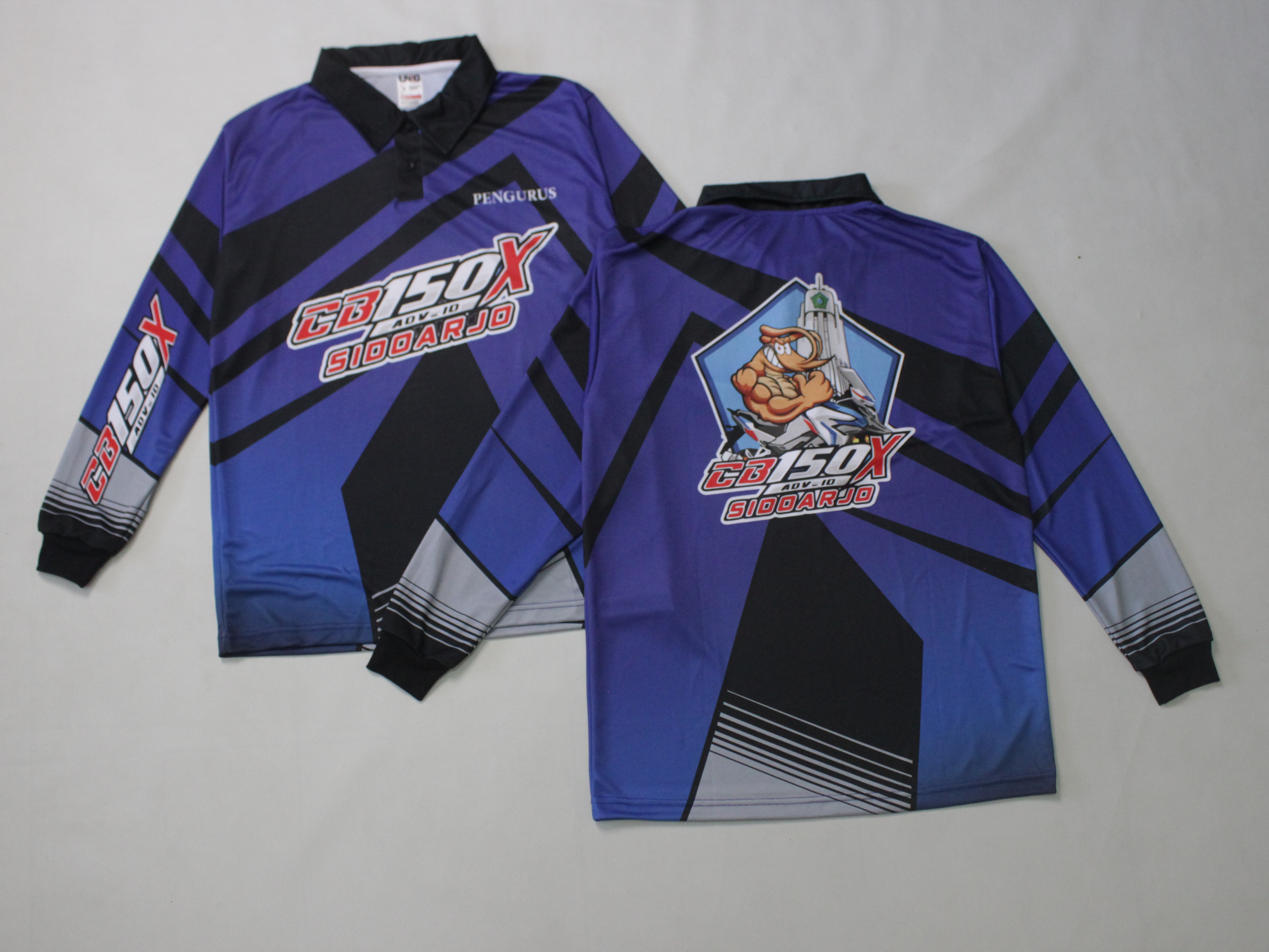 Dua jersey motor lengan panjang biru-hitam diletakkan di latar abu-abu, tampak depan dan belakang: nama komunitas tercetak besar di punggung di bawah lambang maskot