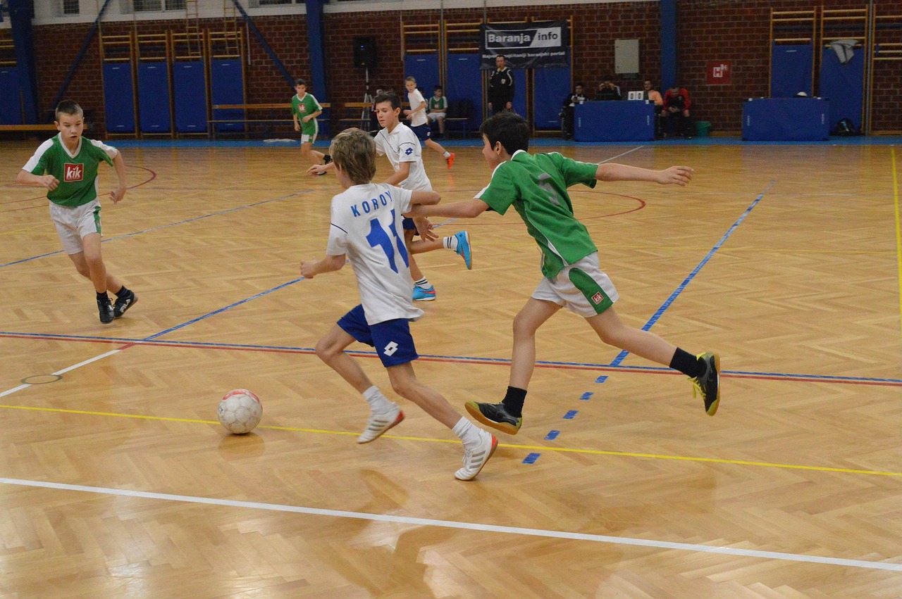 Pemain futsal memakai jersey tim bernomor punggung bertanding di lapangan indoor