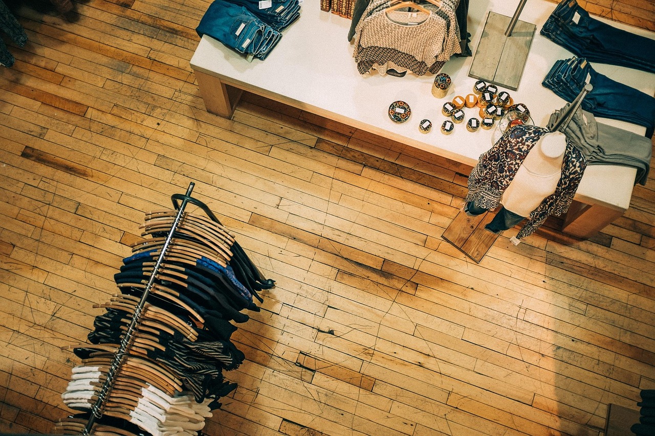 Interior butik pakaian dari atas: rak gantungan kayu berisi kemeja dan rajutan, meja display dengan pakaian terlipat dan manekin