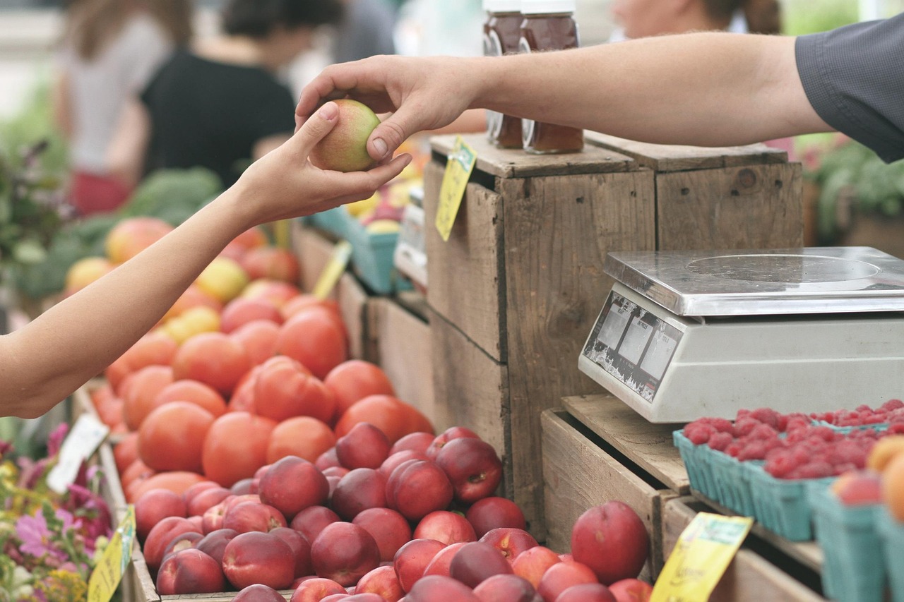 Tangan penjual menyerahkan buah kepada tangan pembeli di kios pasar, di samping timbangan dan label harga