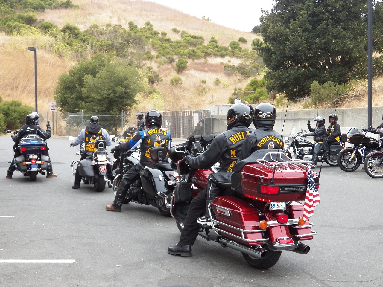 Barisan pengendara berseragam hitam dengan nama klub terbaca di punggung berkumpul bersama motornya di area parkir, dilihat dari belakang