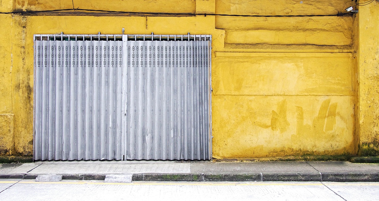 Rolling shutter toko tertutup rapat menutupi pintu, dinding kuning di sisinya