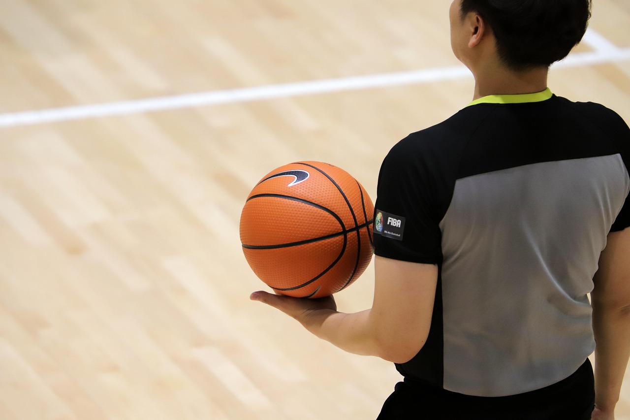Wasit basket berseragam gelap berdiri di sisi lapangan indoor