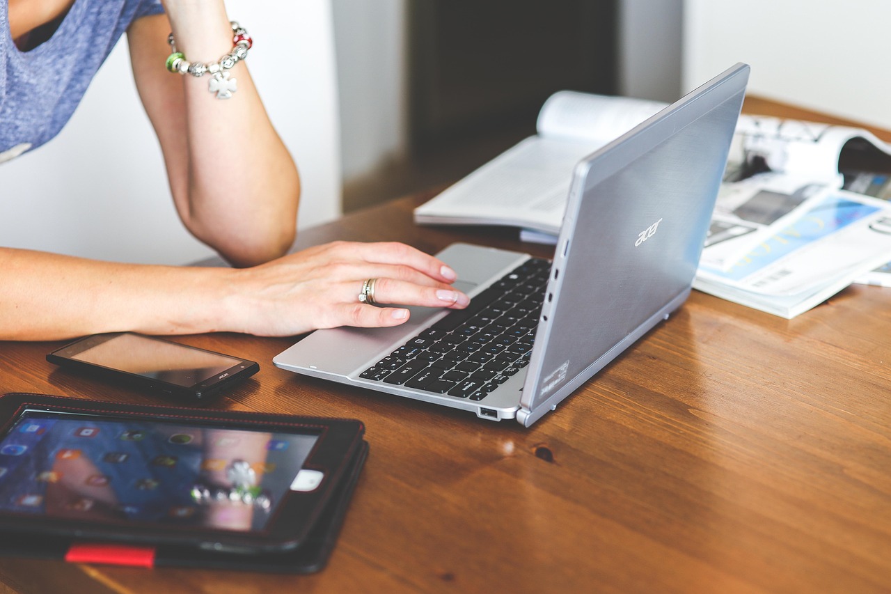 Penjual perempuan bekerja di depan laptop, ponsel dan tablet tergeletak di meja kayu di sampingnya