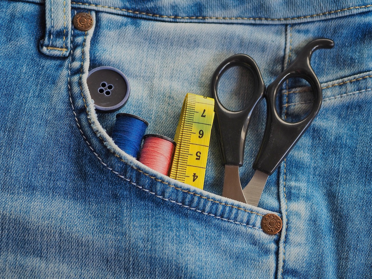 Pita ukur jahit kuning di atas jeans bersama gunting dan benang jahit