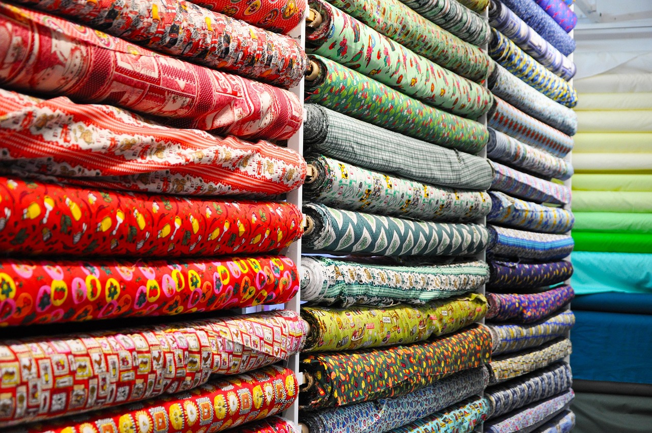 Gulungan kain berbagai warna tersusun per warna di rak toko kain